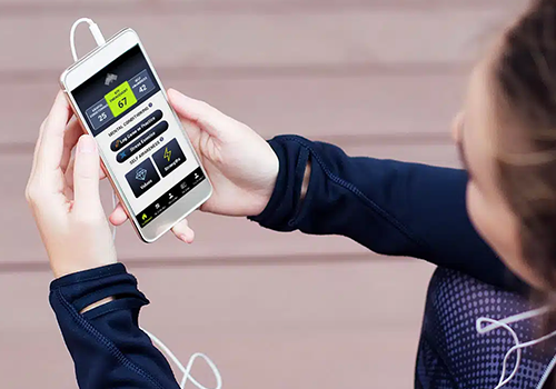 Person outdoors holding a white smartphone that shows a health/fitness app with metrics on the screen.