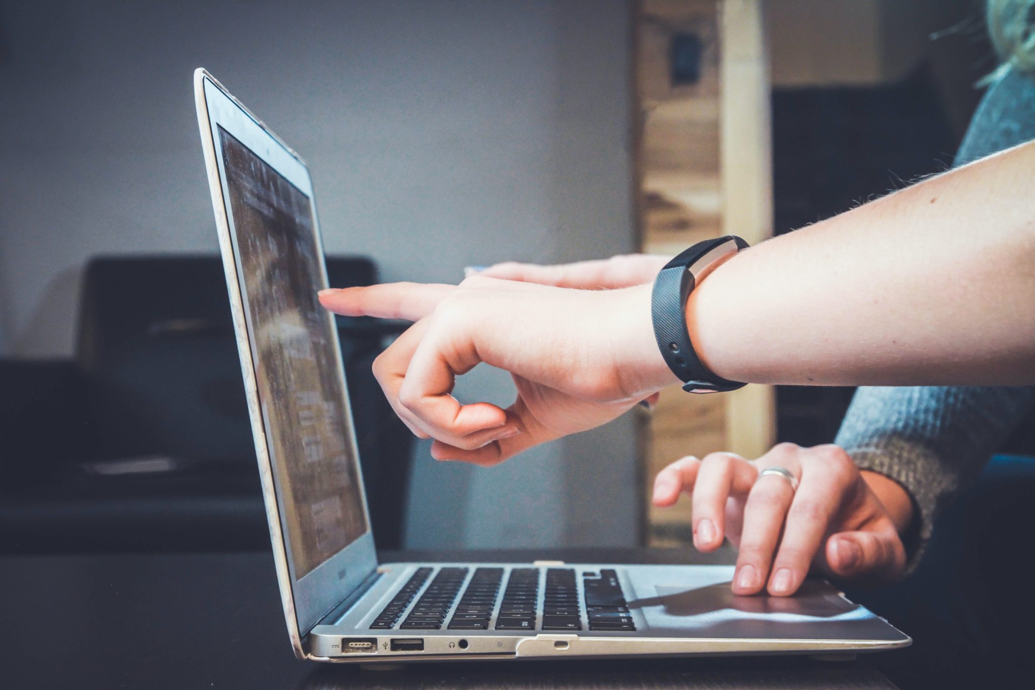 Image of laptop in profile with one hand on the keyboard and another pointing at the screen.