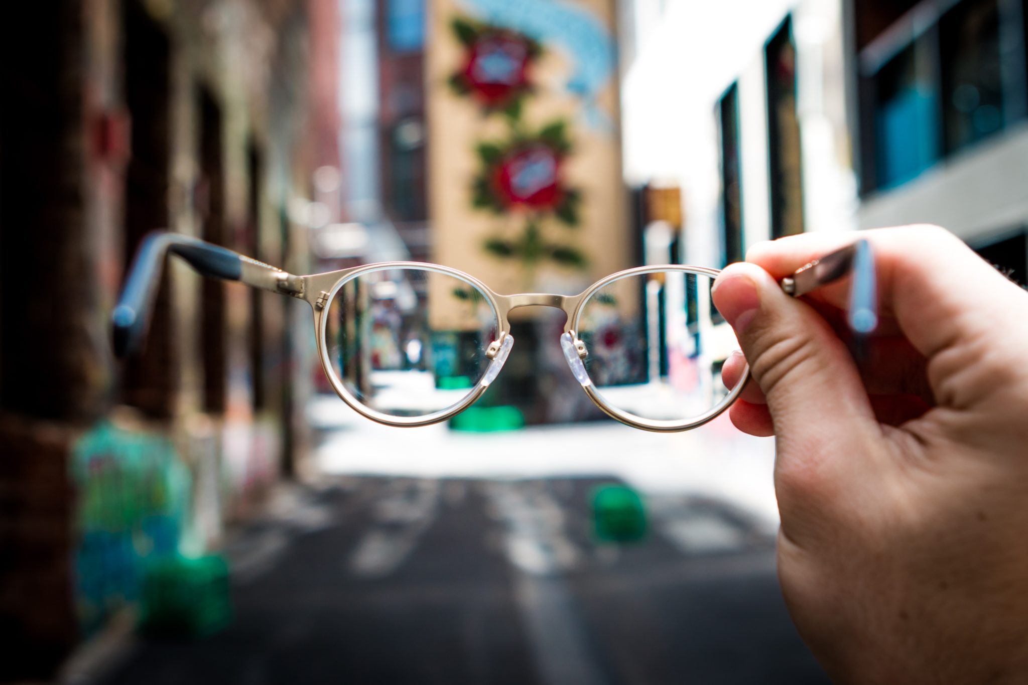 A hand holding eyeglasses with a city street in the background.