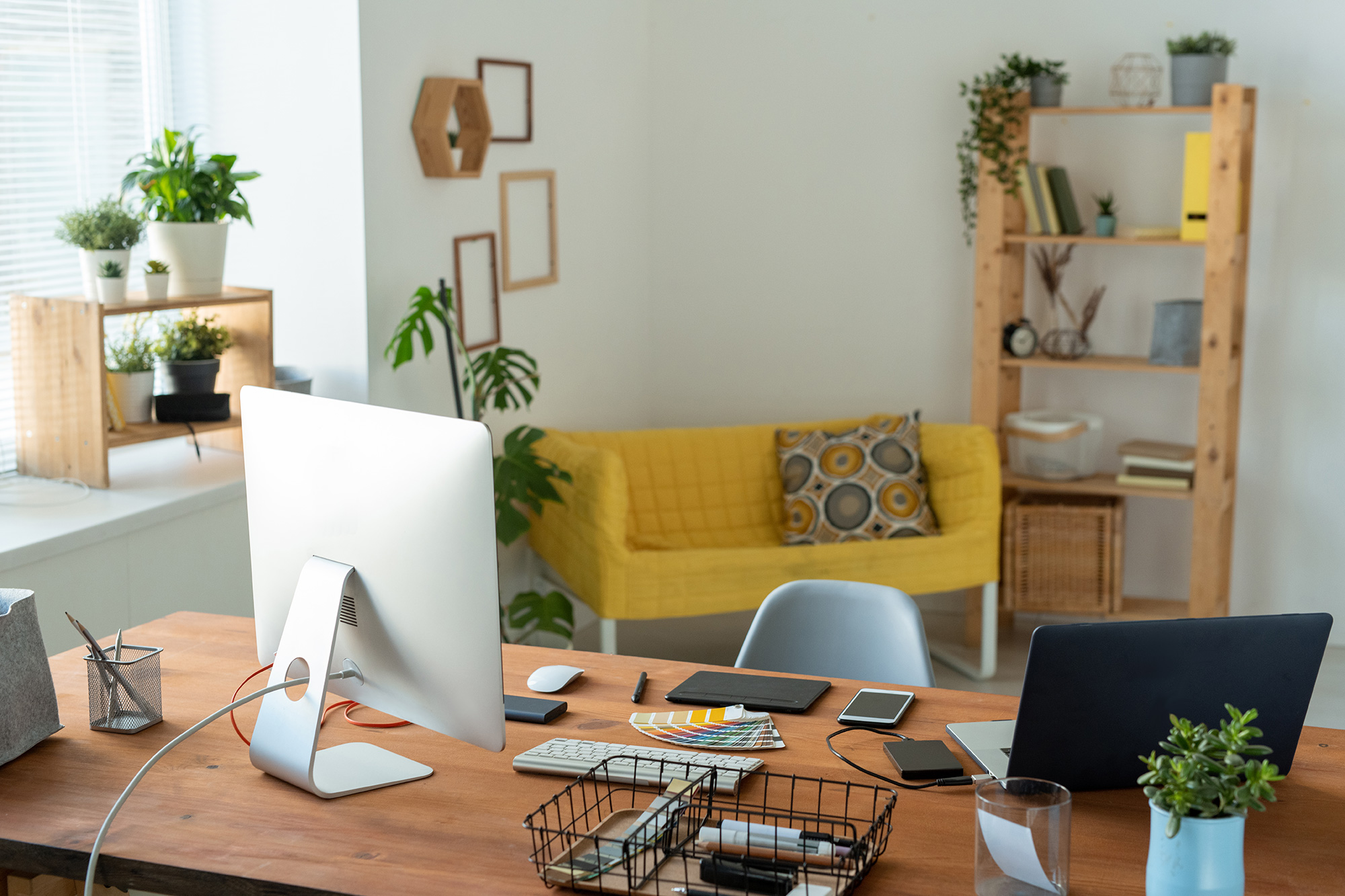 Photo of a home office with a computer and desk in the foreground and yellow couch in the background.