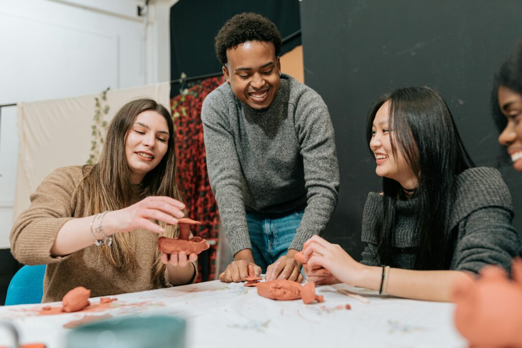 People smiling and molding red clay with their hands.