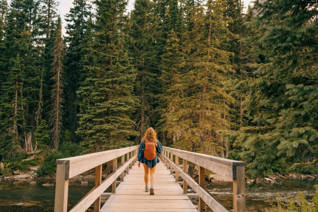 A woman with a backpack crossing a bridge into a forest.