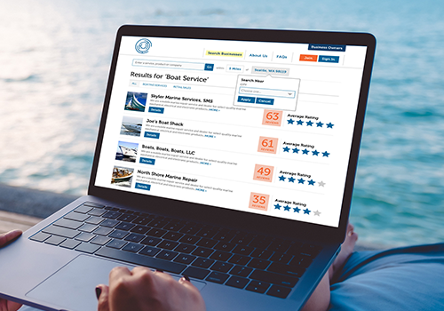 Person using a laptop on a beach, displaying a boat service search results page with listings and ratings.