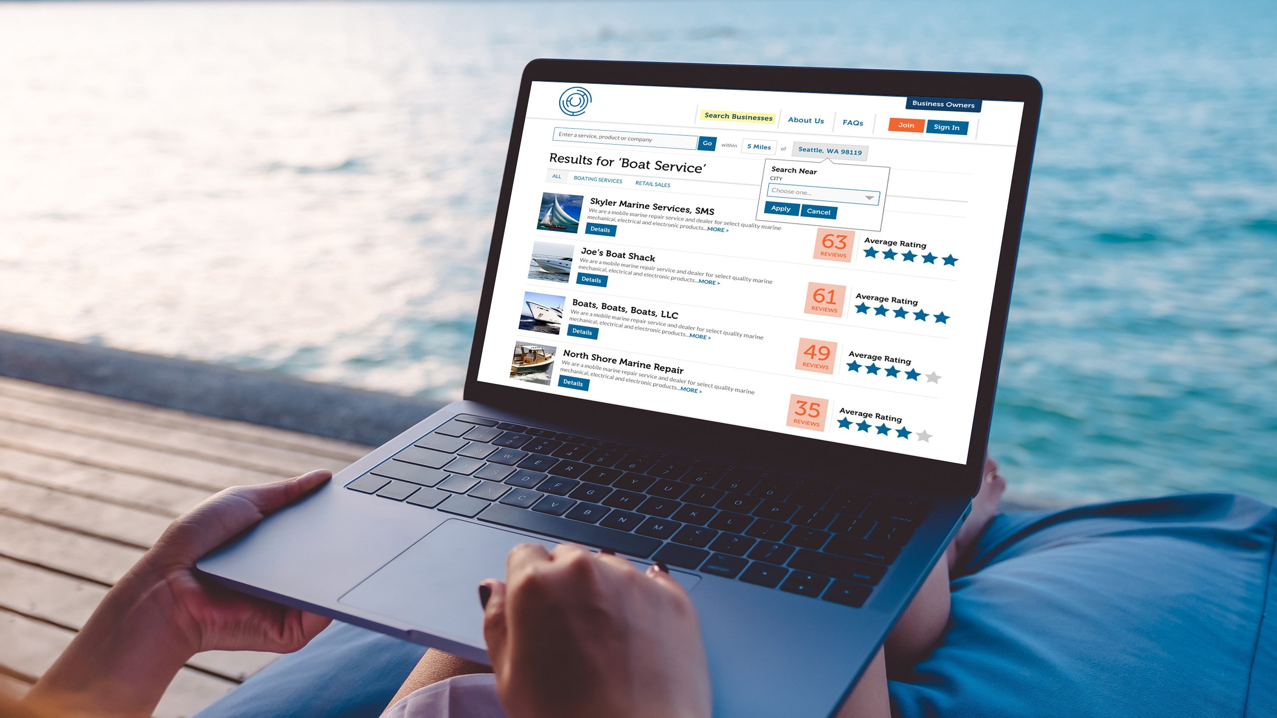Person holding a laptop outdoors by a waterfront, screen displaying a boat services directory with listings and star ratings.
